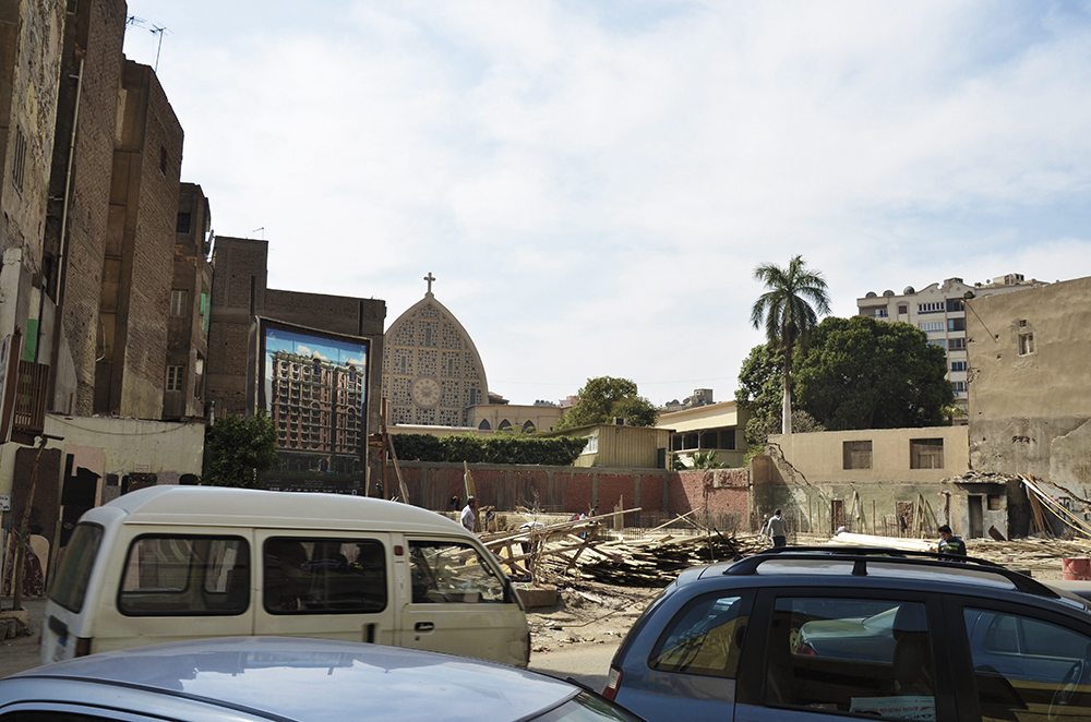 Construction on al-Zāhir St. The poster shows a ten-story building with clothing shops (Levi’s, Mango, and GAP) on the ground floor. In the background is the Church of Collège de la Salle. ©TADAMUN