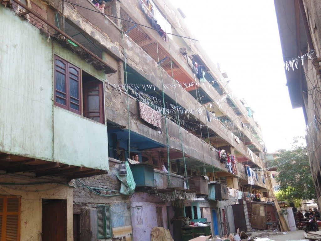 The poor live in poor homes; they do not have enough money for the maintenance of their homes, they do not have the luxury possessions to decorate them, and cannot afford the cost of a flat so they end up dividing the flats into smaller units, where more than one family live in the same unit. This photograph shows one of the recurring government housing patterns within `Azīz `Izzat housing, where there is poverty, urban and color deterioration (Tadamun, 2015)