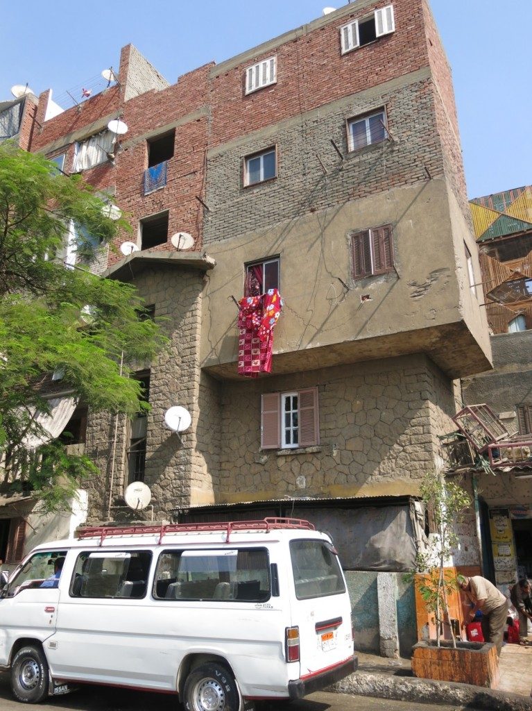 The informal building of additional floors in Laborers town, the original building with its stone façade and the higher floors built in brick are apparent. (Tadamun, 2015)