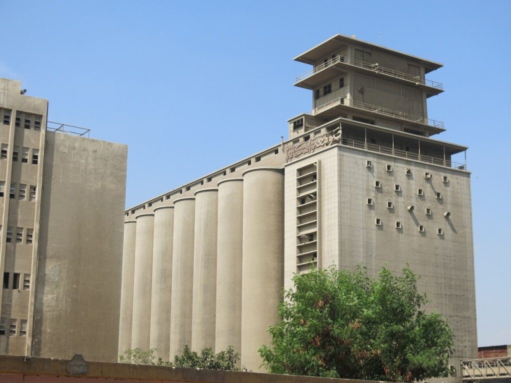Imbāba grain silos – officially North Giza Flour Mills –on the corniche after al-Sāḥil Bridge – for those coming from the direction of Giza – the entrance is on al-Wiḥda Street in Imbāba. The grain silos own a railway line passing through Imbāba to transport the grains, (Tadamun, 2015)